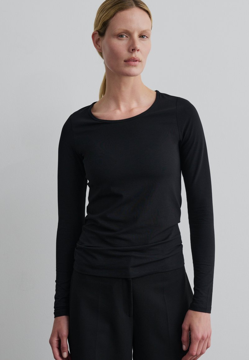 Zwarte langriemtop met een ronde hals, gemaakt van een zachte, stretchy stof. Soepele textuur met een aansluitende pasvorm.