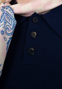 Vêtement en maille bleu marine avec trois boutons noirs et une écharpe à motifs cachemire rose et bleu drapée près du col.