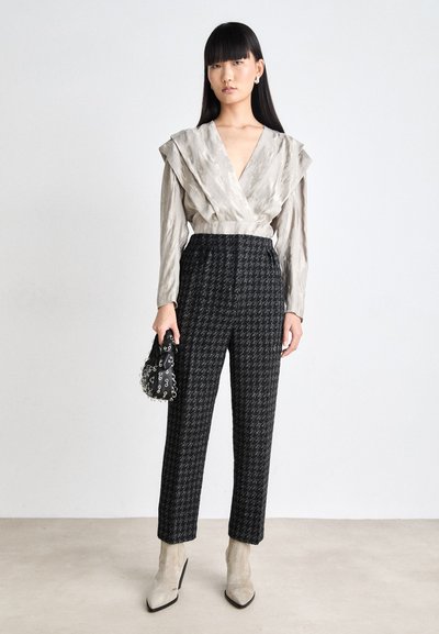 Top gri cu un model elegant, cu pliuri dramatice la umeri, asortat cu pantaloni cu model houndstooth alb-negru și botine bej până la glezne. Geantă neagră cu accente.