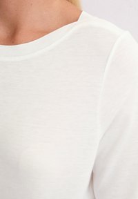 Weißes Baumwoll-T-Shirt mit rundem Halsausschnitt und eingesetzten Ärmeln; der Stoff hat eine glatte Textur; minimales Design ohne sichtbare Muster oder Akzente.