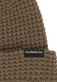 Gorro de punto en verde oliva oscuro con un patrón texturizado y una etiqueta negra que presenta texto en blanco.