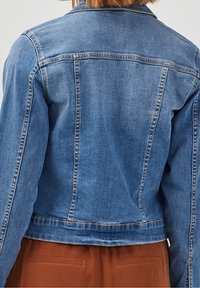 Veste en denim bleu avec un design court, des coutures visibles et un col classique. Elle possède un dos à empiècement et une coupe ajustée.