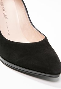 Chaussure à talon haut en suède noir avec un bout pointu et une semelle en cuir verni lisse. Texture douce avec une doublure intérieure légèrement brillante.