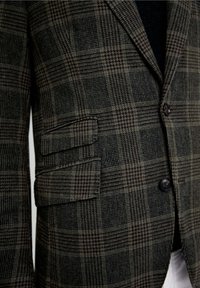 Blazer de cuadros en tonos verde oscuro y marrón. Presenta solapas afiladas, dos bolsillos frontales y botones oscuros. Tejido texturizado con patrón a rayas.