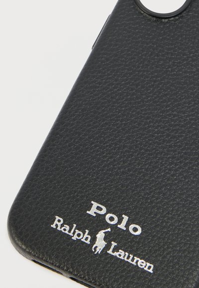Κοντινό πλάνο μαύρης υφής δερμάτινης θήκης τηλεφώνου με το ασημένιο λογότυπο Polo Ralph Lauren και το έμβλημα ποδηλάτη του πόλο κοντά στο κάτω μέρος.