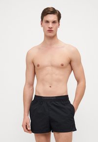 Pantaloni da nuoto neri con una texture morbida e leggera. La vita elastica presenta un logo Calvin Klein. Le tasche laterali sono integrate nel design.