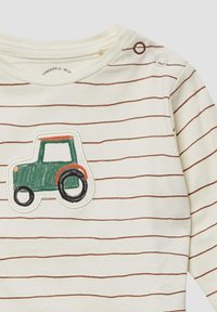 Cremefarbendes Langarmshirt mit braunen horizontalen Streifen. Verfügt über eine grüne Traktor-Stickerei, akzentuiert mit Orange und Schwarz. Druckknöpfe an der Schulter.