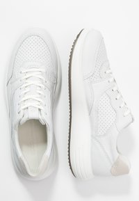 Para białych skórzanych sneakersów z perforowanymi detalami, sznurowanym zapięciem i grubą gumową podeszwą na białym tle.