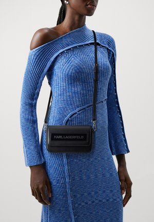 Blauwe geribbelde gebreide jurk met een off-shoulder ontwerp, voorzien van gestructureerde lijnen. Zwarte crossbody tas met logo en slanke hardware details.