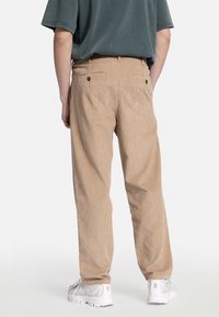 Beige kordfløyelsbukser med komfortabel passform, synlige sømmer og to baklommer. Modellen har på seg hvite sneakers.