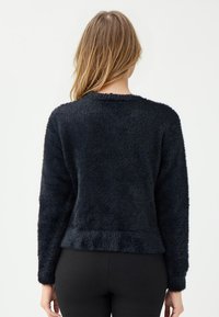 Maglione nero, con texture, maniche lunghe e scollatura rotonda. Tessuto morbido e peloso, con un taglio leggermente corto e orlo a coste.