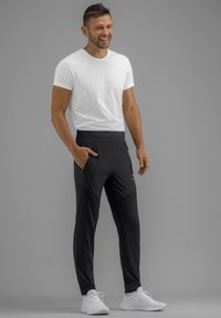 Witte t-shirt en zwarte sportbroek met een taps design, voorzien van zijzakken en een comfortabele tailleband. Witte sneakers.