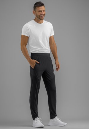 Weißes T-Shirt und schwarze Sporthosen mit tailliertem Design, ausgestattet mit seitlichen Taschen und einem bequemen Bund. Weiße Sneakers.