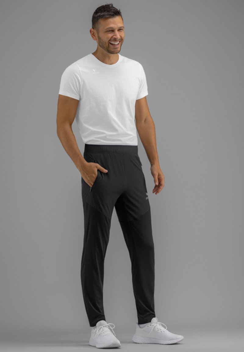 Witte t-shirt en zwarte sportbroek met een taps design, voorzien van zijzakken en een comfortabele tailleband. Witte sneakers.