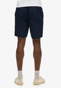 Shorts bleu marine avec des pois blancs, taille élastique, deux poches latérales et une poche arrière. Tissu léger avec une finition texturée.