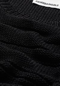 Black knitted sweater fabric with a textured pattern, featuring a ribbed design at the collar. The brand label reads "ARMEDANGELS."