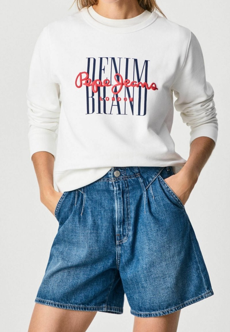 Felpa bianca con grafica "DENIM BRAND" in blu e rosso, abbinata a pantaloncini di jeans blu con design classico delle tasche e vestibilità comoda.