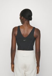 Crop top sportivo nero con scollo a V, texture liscia e logo Nike sul davanti. Abbinato a pantaloni jogger chiari.