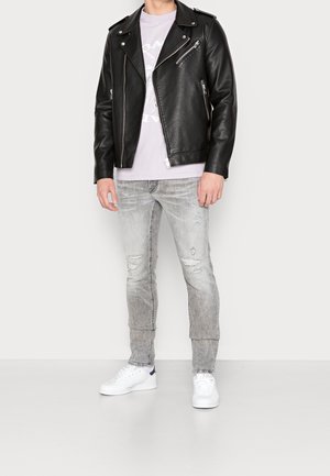 Zwarte leren bikerjack met zilveren ritsen, gedragen over een lichtpaarse T-shirt. Grijze versleten spijkerbroek en witte sneakers maken de outfit compleet.