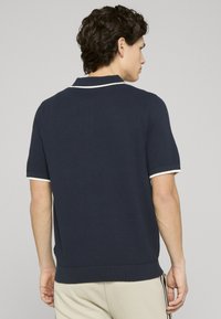 Polo à manches courtes bleu marine avec tissu texturé, passepoil blanc sur le col et les manches, ourlet côtelé et coupe décontractée.