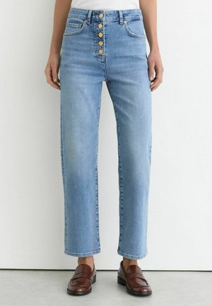 Lyseblå jeans med høj talje og lige ben med fem synlige knapper foran, båret med brune læder loafers og en hvid top.