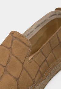 Ταμπά μοκασίνι από σουέντ με τετράγωνο ανάγλυφο σχέδιο και ραφές κατά μήκος της σόλας, που δείχνει κοντινή όψη του άνω μέρους και του ανοίγματος.