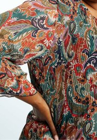 Robe florale colorée avec une texture plissée. Présente des motifs vibrants en rouge, vert et bleu. Manches ballon et col rond.