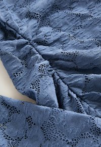 Tessuto di pizzo in azzurro tenue con motivi floreali intricati; presenta sezioni arricciate e una finitura testurizzata.