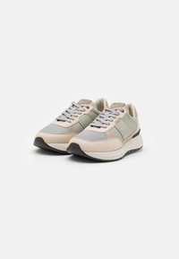 Sneaker aus einer Mischung von Mesh- und Wildledermaterialien in einem beige-hellgrauen Farbschema, mit schwarzer Sohle und dezentem Branding.