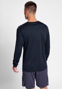 Langärmliges Sportshirt in Marineblau mit Rundhalsausschnitt und gemusterten Akzenten an den Schultern, kombiniert mit dunklen Shorts.
