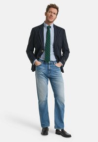 Mørkeblå stribede blazer med guldknapper, lyseblå skjorte, grøn stribet slips, lyseblå jeans og skinnende sorte loafers.