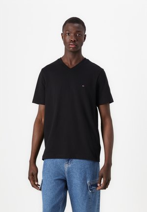 Tricou negru cu decolteu în V, confecționat din bumbac, cu mâneci scurte și un logo mic brodat pe piept. Asortat cu blugi din denim albastru.