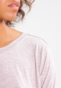 Ljuslila kortärmad topp med en mjuk textur, bred halsringning och subtil sömdekor längs axeln och halsringningen.