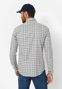 Karierte Hemd mit blauen, braunen und cremefarbenen Mustern; lange Ärmel mit Knopfmanschetten; abgerundeter Saum; kombiniert mit dunkelblauen Jeans.