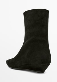 Stivaletto alla caviglia in suede nero con tacco a zeppa basso e punta appuntita, mostrato su sfondo bianco.