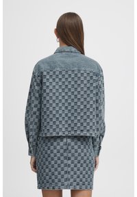 Komplet kurtka jeansowa i spódnica w jasnoszarym kolorze z wzorem w kratę. Posiada kołnierz, długie rękawy oraz zapięcie na guziki z przodu.