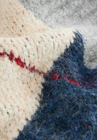 Knitted wool blanket in cream, navy, and red. Features varied textures with a loose weave, showcasing soft, fuzzy fibers and a geometric pattern.