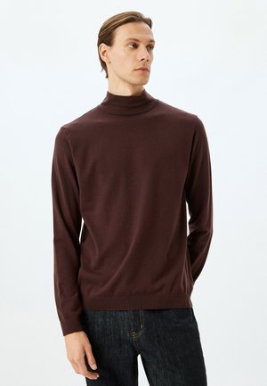 Maglione dolce a collo alto di colore marrone, realizzato in morbido tessuto a maglia, con maniche lunghe e orlo a costine, abbinato a jeans in denim scuro.
