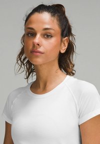 Weißes Sport-T-Shirt mit gerippter Textur, kurzen Ärmeln und rundem Ausschnitt. Der Stoff ist leicht und figurbetont.
