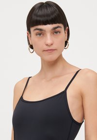 Black swimwear with thin straps, a square neckline, and a smooth texture. Features subtle stitching details on the sides.