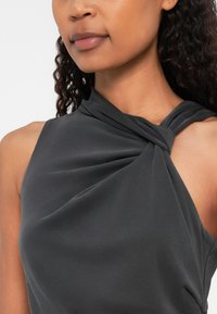 Siva bezrukava majica s detaljem uvrnutog čvora na ramenu, izrađena od glatkog materijala, sa preklopnim dizajnom.