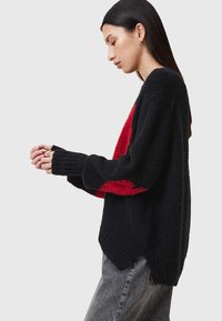 Strickpullover mit schwarzem Körper und kräftigem roten Akzent, lockerer Passform, gerippten Bündchen und einem leicht abgerundeten Saum. Weiches, strukturiertes Material.
