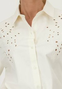 Witte button-up shirt met geborduurde bloempatronen en uitsnijdingen op de schouders. Zachte stof, getailleerde pasvorm.