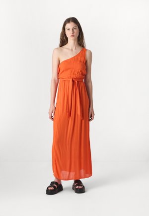 Enaxlad, golvlång orange klänning med insvängd midja och knytdetalj. Modell som bär kraftiga svarta platåsandaler.