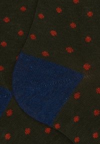 Dunkelgrüne Socken mit kleinen roten Punkte und einfarbigen blauen Fersen, die die Stoffstruktur und das Strickmuster zeigen.