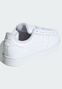 Bijela kožna tenisica s glatkim završetkom, s tri perforirane pruge, okruglim vrhom, bijelim vezicama i teksturiranim potplatom.