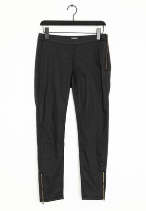 Black slim-fit pants with side and ankle gold zippers, hanging on a black hanger against a white background.