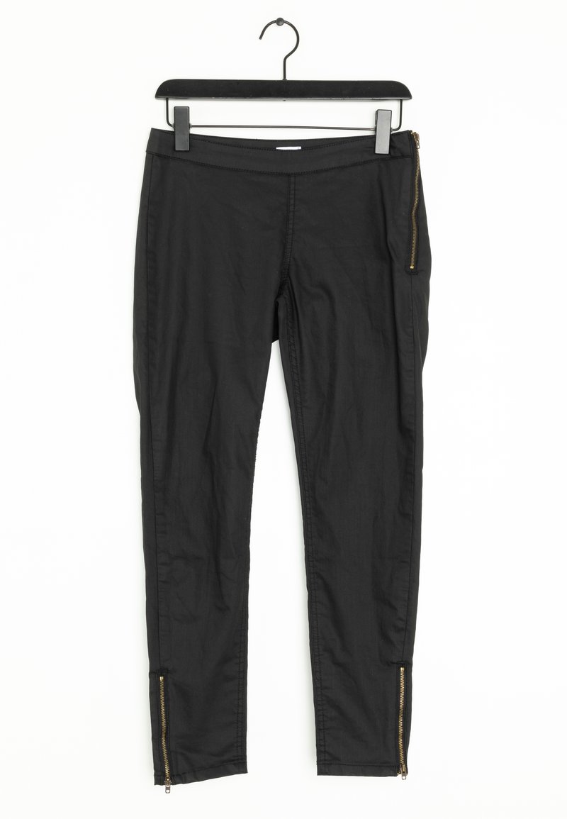 Pantalon noir slim avec fermetures éclair dorées sur les côtés et aux chevilles, suspendu à un cintre noir sur un fond blanc.