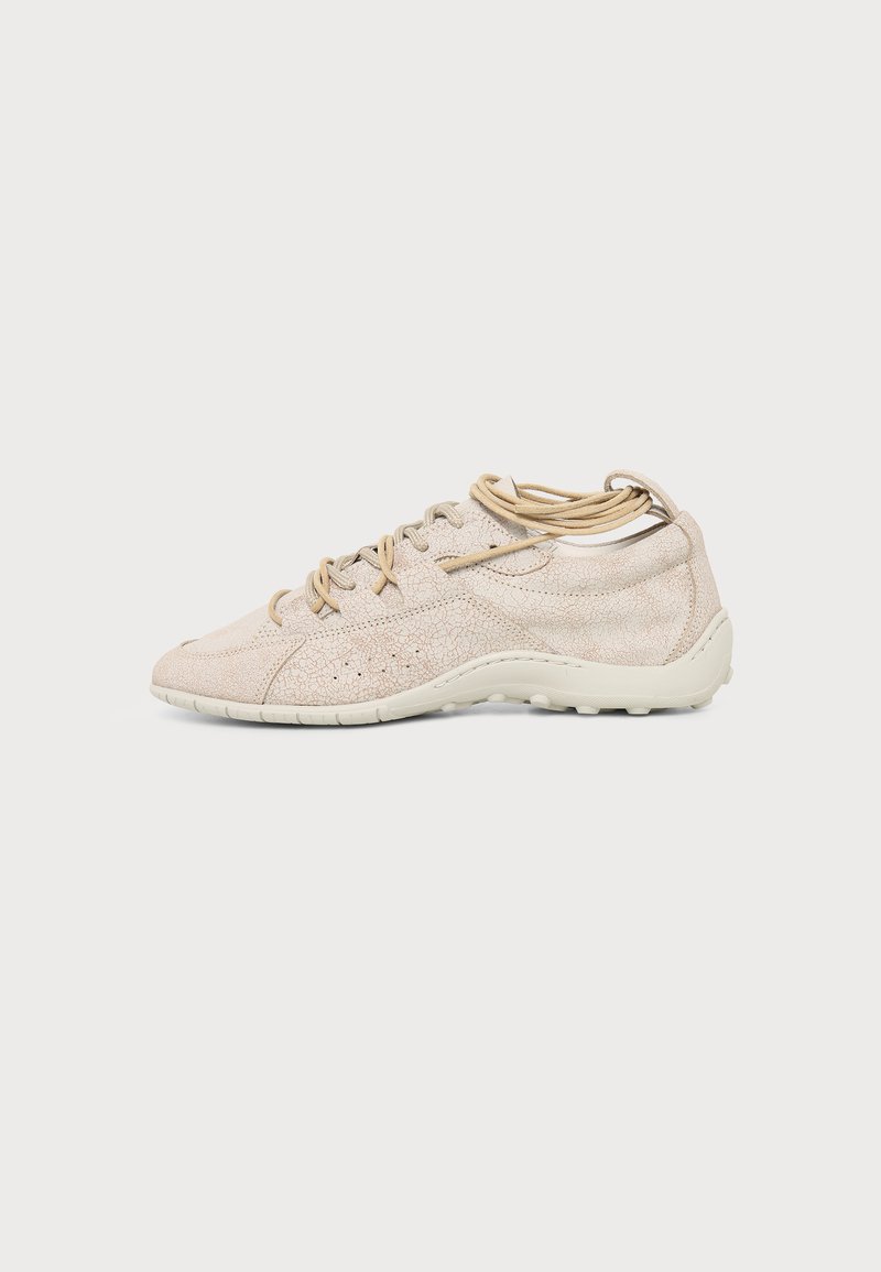 Ανοιχτό μπεζ casual sneaker με υφασμάτινη επιφάνεια, σχεδιασμό με κορδόνια και λευκή ελαστική σόλα, εμφανίζεται από το πλάι σε απλό φόντο.