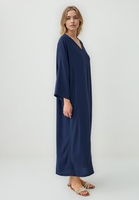 Abito maxi blu navy con scollo a V, maniche ampie e vestibilità rilassata. Realizzato in tessuto leggero, con una texture liscia.